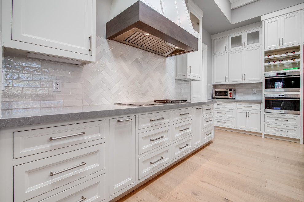 Inspiration for a large transitional l-shaped light wood floor, white floor and tray ceiling eat-in kitchen remodel in San Francisco with an undermount sink, white cabinets, quartz countertops, gray backsplash, ceramic backsplash, stainless steel appliances, an island and gray countertops