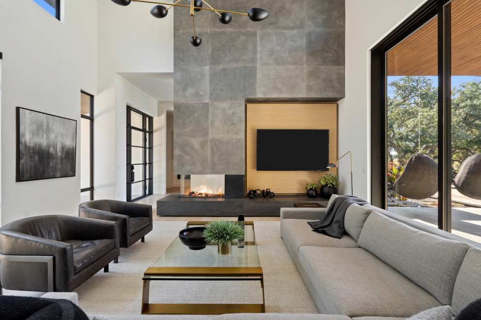 Esempio di un soggiorno minimal con pareti grigie, parquet chiaro, camino bifacciale, cornice del camino in cemento, TV a parete e pavimento beige
