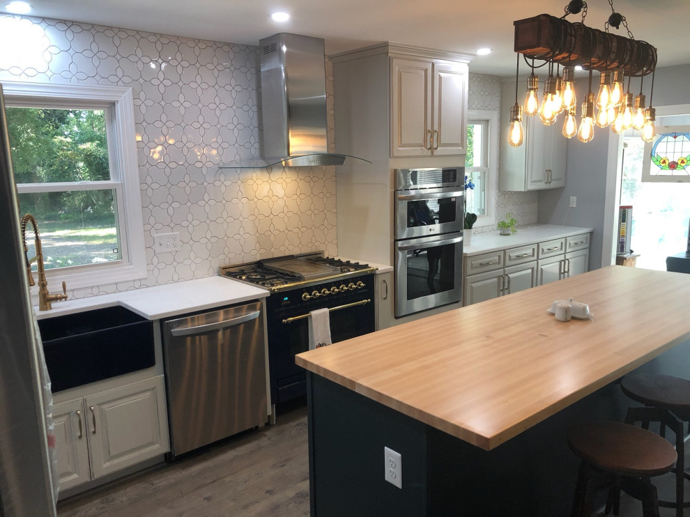 Mid-sized transitional l-shaped vinyl floor and brown floor kitchen photo in DC Metro with a farmhouse sink, raised-panel cabinets, gray cabinets, solid surface countertops, white backsplash, ceramic backsplash, stainless steel appliances, an island and white countertops