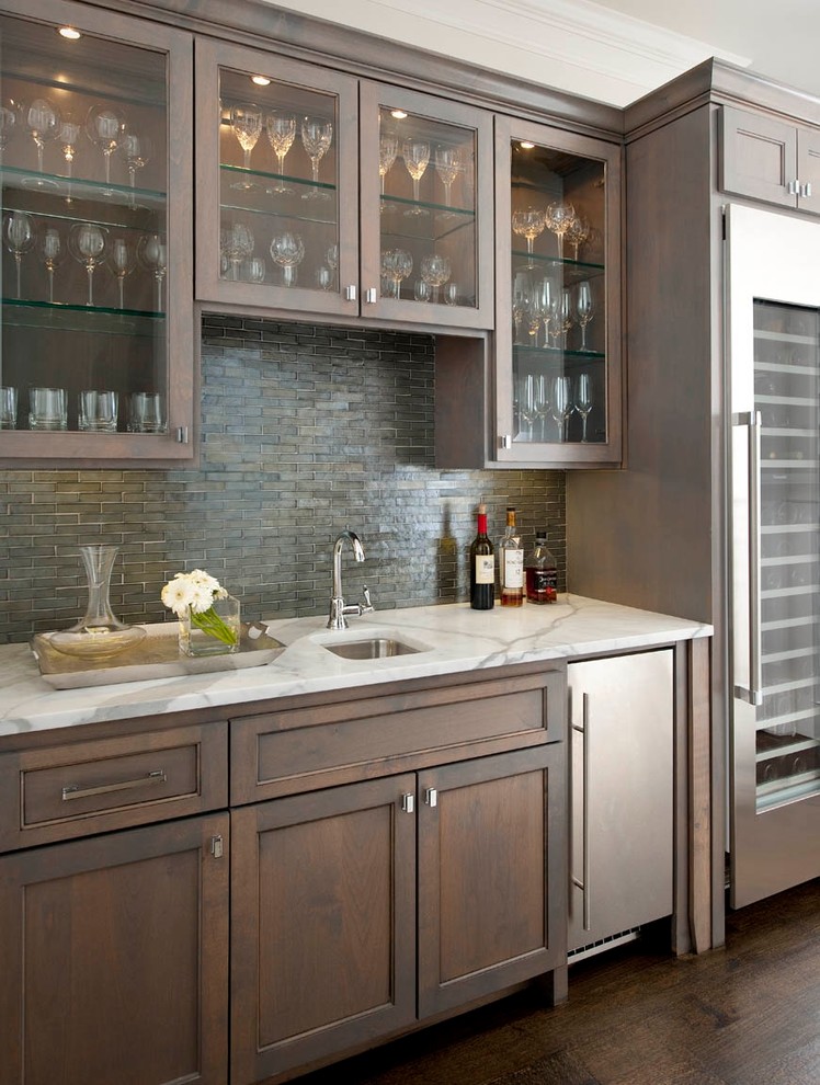 Photo of a traditional single-wall wet bar in Dallas with dark hardwood floors, an undermount sink, recessed-panel cabinets, dark wood cabinets, grey splashback, matchstick tile splashback, brown floor and white benchtop.