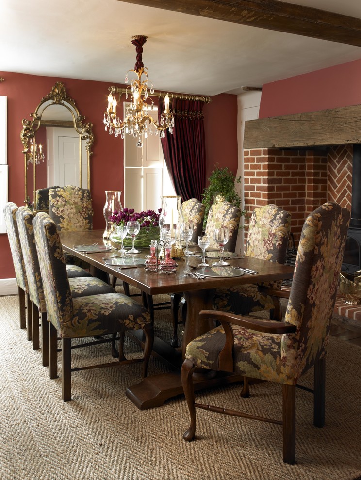 This is an example of a country separate dining room in London with red walls, a wood stove, a brick fireplace surround and carpet.