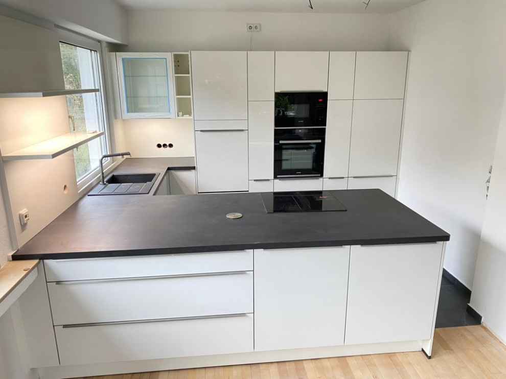 Inspiration for a mid-sized contemporary u-shaped open plan kitchen in Other with white cabinets, wood benchtops, white splashback, timber splashback, black appliances, with island, black floor and black benchtop.