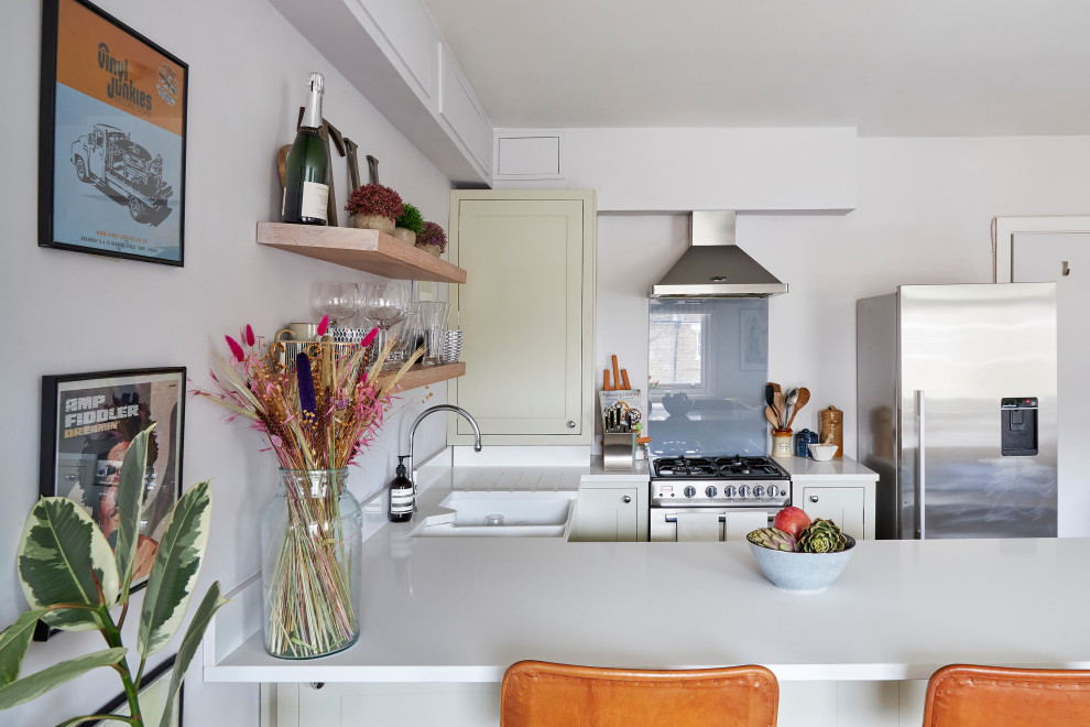 Inspiration for a small classic u-shaped open plan kitchen in London with a belfast sink, recessed-panel cabinets, green cabinets, composite countertops, white splashback, glass sheet splashback, stainless steel appliances, dark hardwood flooring, a breakfast bar, brown floors and white worktops.