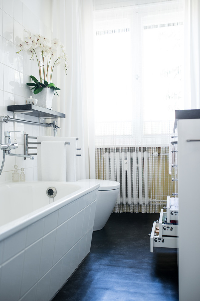 This is an example of a small contemporary bathroom in Berlin with white cabinets, a drop-in tub, white tile, ceramic tile, an integrated sink, black floor, flat-panel cabinets, a one-piece toilet, white walls, linoleum floors and black benchtops.