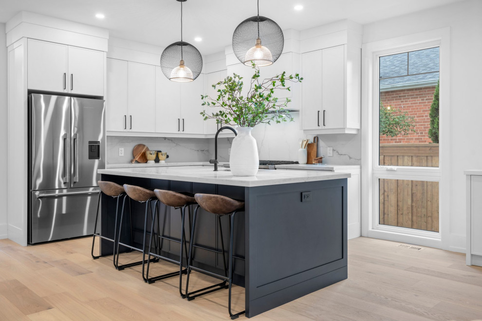 Open concept kitchen - mid-sized transitional l-shaped light wood floor open concept kitchen idea in Toronto with an undermount sink, flat-panel cabinets, white cabinets, quartz countertops, white backsplash, quartz backsplash, stainless steel appliances, an island and white countertops