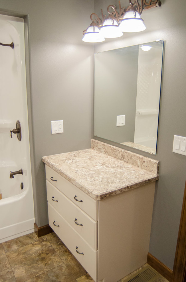 This is an example of a mid-sized traditional 3/4 bathroom in Other with raised-panel cabinets, white cabinets, a drop-in tub, a shower/bathtub combo, a two-piece toilet, grey walls, medium hardwood floors, a drop-in sink and granite benchtops.