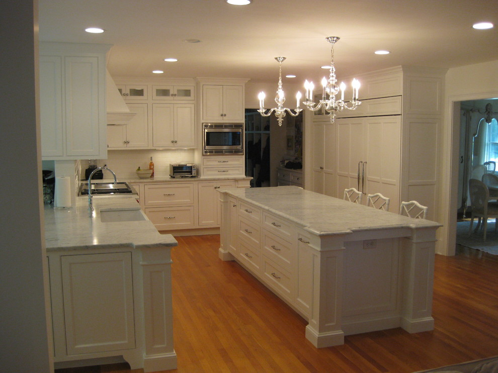 Inspiration for a transitional u-shaped medium tone wood floor eat-in kitchen remodel in Boston with a farmhouse sink, beaded inset cabinets, white cabinets, marble countertops, white backsplash, subway tile backsplash, stainless steel appliances and an island