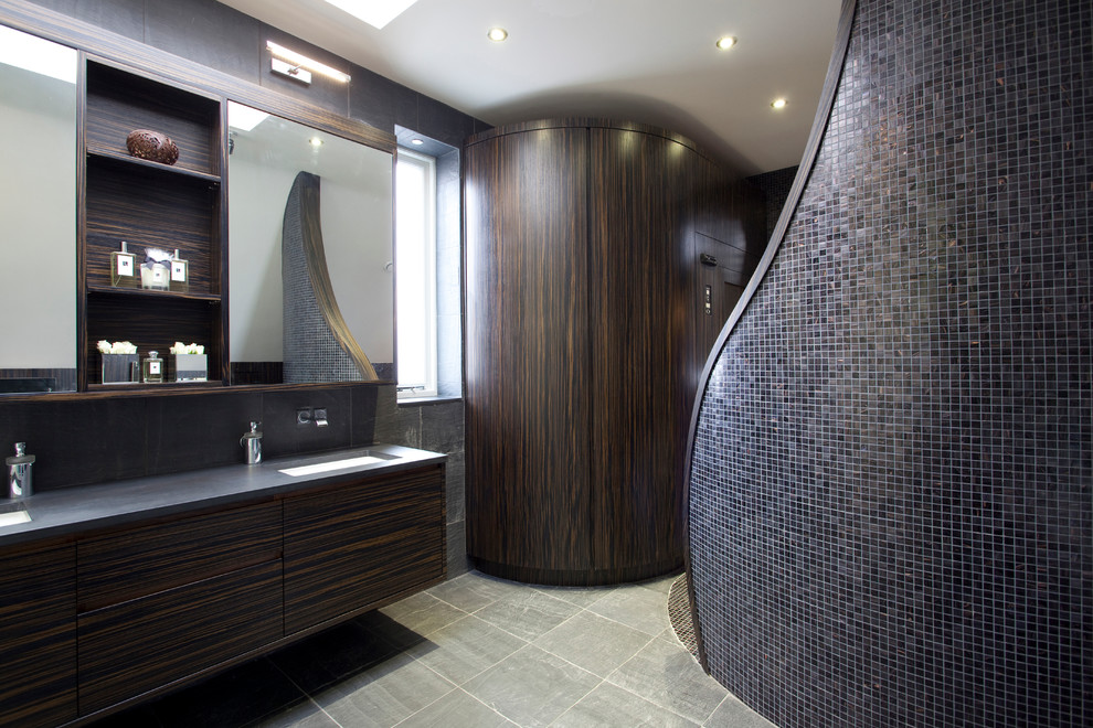 Mid-sized contemporary bathroom in London with an undermount sink, flat-panel cabinets, dark wood cabinets, solid surface benchtops, a freestanding tub, a one-piece toilet, gray tile, mosaic tile, white walls and ceramic floors.