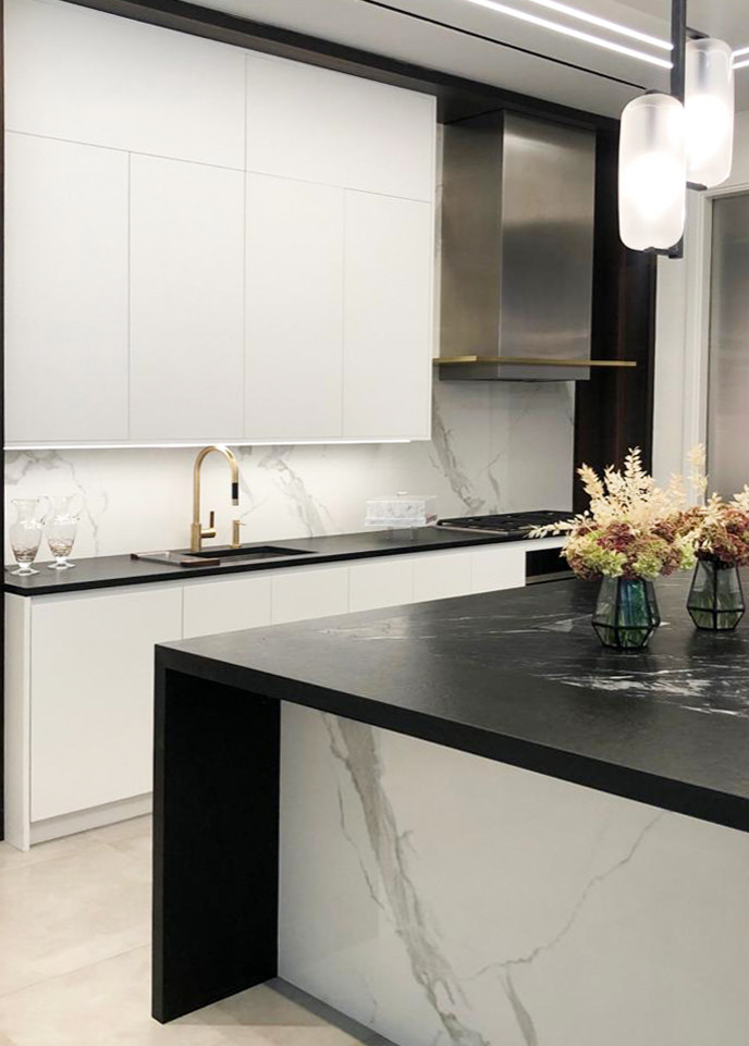 Large modern u-shaped eat-in kitchen in New York with an undermount sink, flat-panel cabinets, white cabinets, marble benchtops, white splashback, marble splashback, black appliances, porcelain floors, with island, beige floor, black benchtop and recessed.