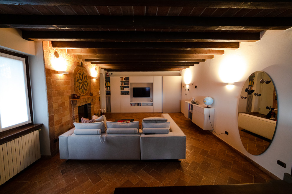 This is an example of a large country formal loft-style living room in Milan with white walls, terra-cotta floors, a standard fireplace, a wall-mounted tv, multi-coloured floor, timber and brick walls.