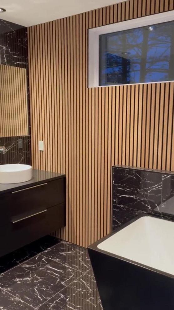 This is an example of a medium sized contemporary ensuite bathroom in Montreal with flat-panel cabinets, black cabinets, a built-in bath, a one-piece toilet, black and white tiles, marble tiles, black walls, marble flooring, a vessel sink, laminate worktops, black floors, black worktops, a single sink, a floating vanity unit and wood walls.