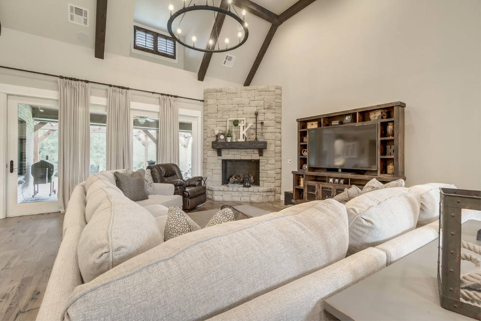 This is an example of a large country open concept family room in Oklahoma City with grey walls, medium hardwood floors, a corner fireplace, a stone fireplace surround and a freestanding tv.