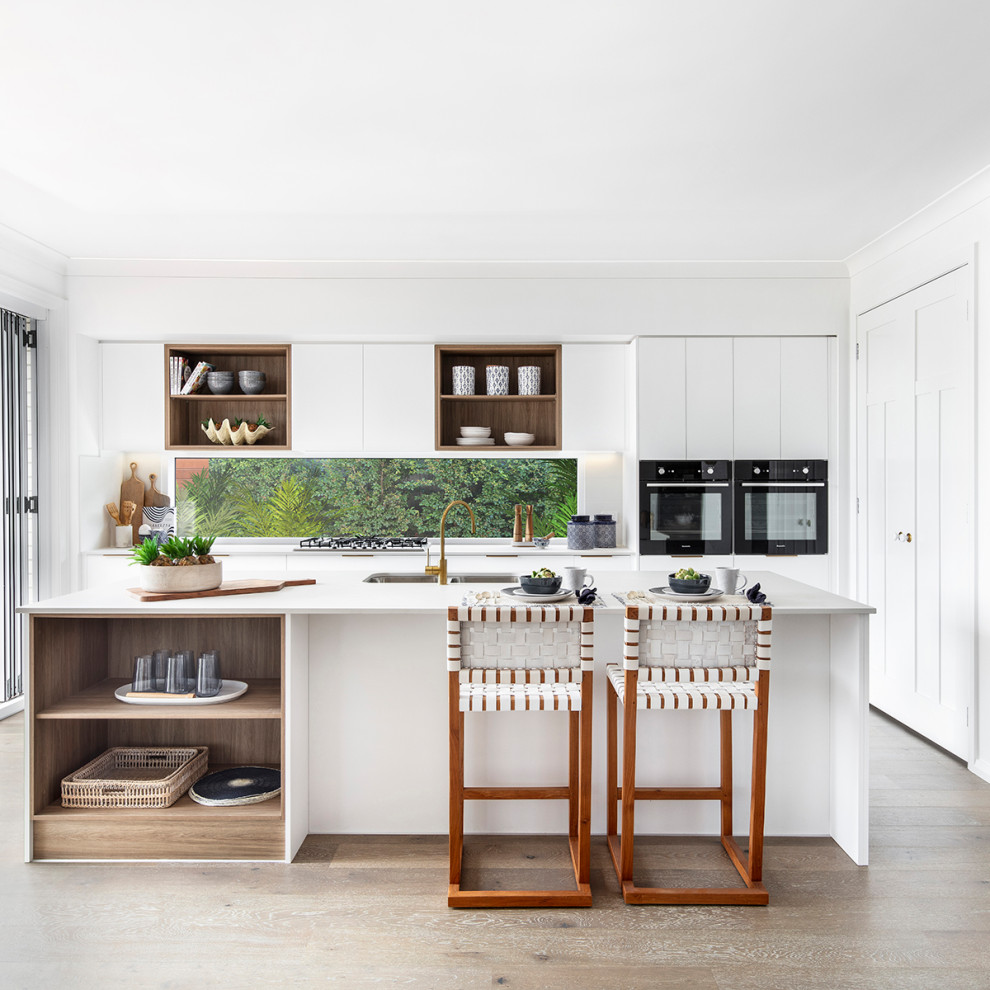 This is an example of a mid-sized beach style l-shaped kitchen pantry in Wollongong with shaker cabinets, white cabinets, quartz benchtops, white splashback, ceramic splashback, light hardwood floors, with island, brown floor and white benchtop.
