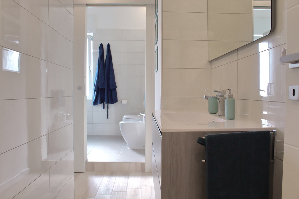 Design ideas for a mid-sized contemporary 3/4 bathroom in Bari with recessed-panel cabinets, medium wood cabinets, a curbless shower, a two-piece toilet, white tile, porcelain tile, white walls, porcelain floors, an integrated sink, solid surface benchtops, beige floor and a sliding shower screen.