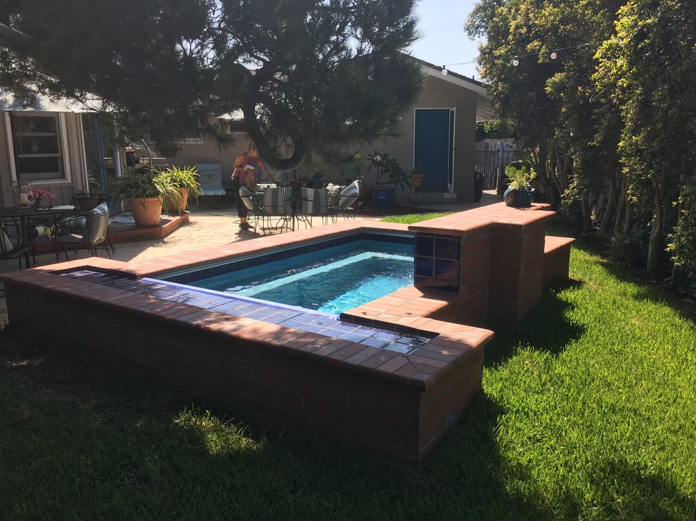 Small traditional backyard rectangular pool in Orange County with a water feature and brick pavers.