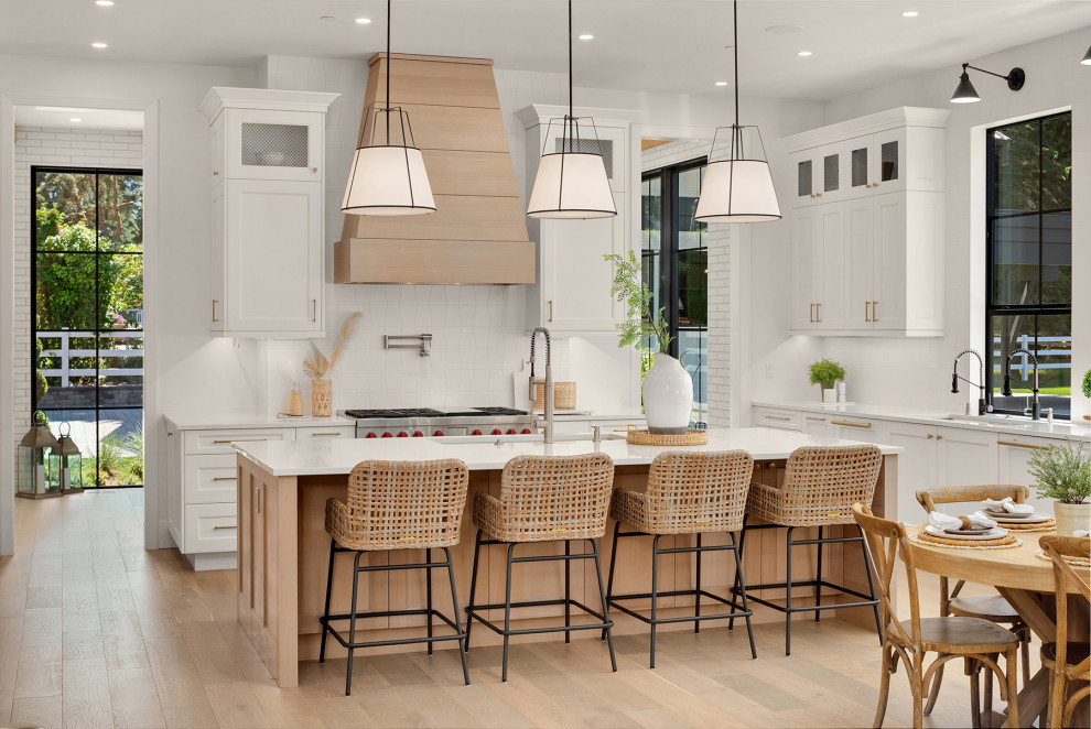 Design ideas for an expansive traditional kitchen/diner in Seattle with a submerged sink, recessed-panel cabinets, light wood cabinets, engineered stone countertops, white splashback, porcelain splashback, integrated appliances, light hardwood flooring, an island and white worktops.