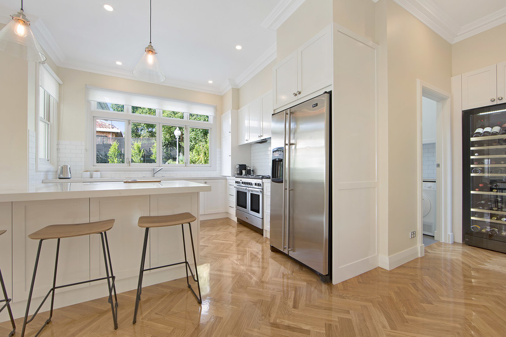 Inspiration for a mid-sized scandinavian eat-in kitchen in Melbourne with white cabinets, white splashback, subway tile splashback, stainless steel appliances, light hardwood floors and with island.