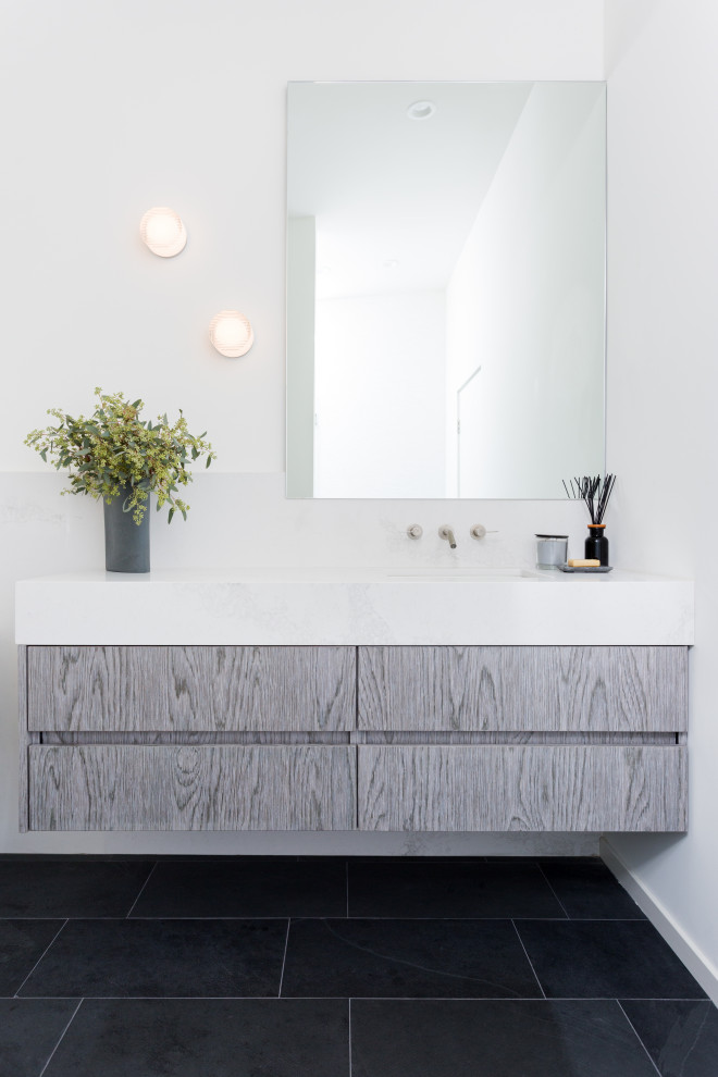 Photo of a mid-sized modern bathroom in Los Angeles with flat-panel cabinets, medium wood cabinets, a one-piece toilet, white tile, stone slab, white walls, slate floors, an undermount sink, engineered quartz benchtops, grey floor, white benchtops, a single vanity, a floating vanity and vaulted.