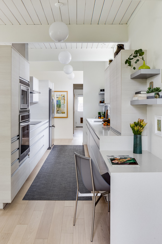 Inspiration for a mid-sized midcentury galley eat-in kitchen in San Francisco with light hardwood floors, beige floor, an undermount sink, flat-panel cabinets, stainless steel appliances, solid surface benchtops, white cabinets, white benchtop, multi-coloured splashback, mosaic tile splashback and timber.