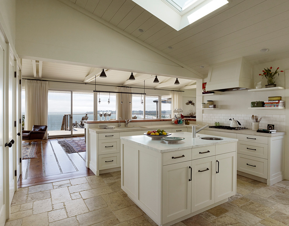 This is an example of a large beach style u-shaped open plan kitchen in San Francisco with an undermount sink, shaker cabinets, white cabinets, quartzite benchtops, white splashback, subway tile splashback, stainless steel appliances, ceramic floors, with island and beige floor.