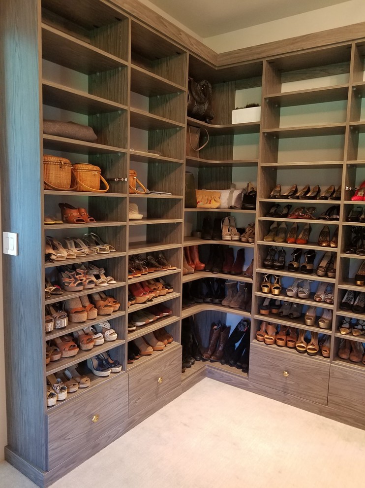 This is an example of a large transitional gender-neutral walk-in wardrobe in New York with open cabinets, dark wood cabinets, carpet and beige floor.