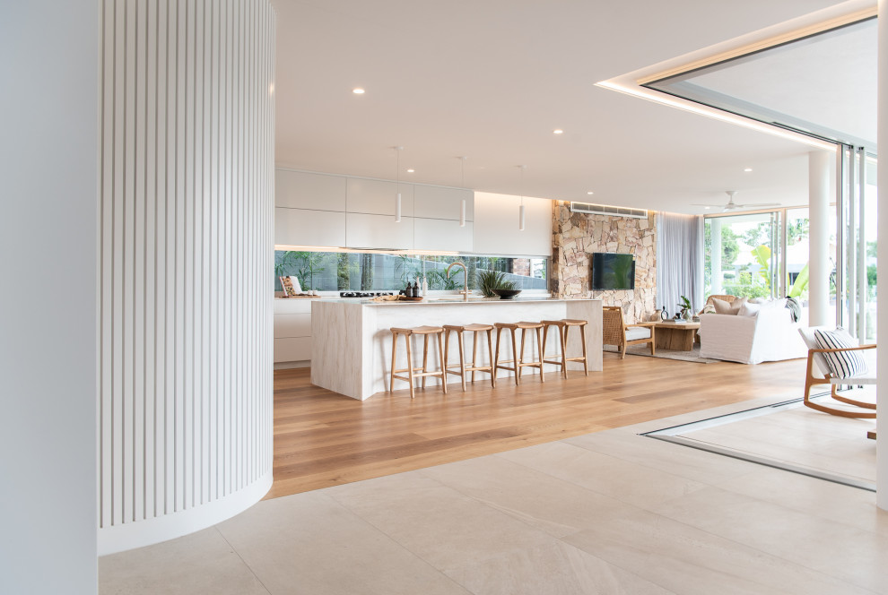 Inspiration for a contemporary galley open plan kitchen in Sunshine Coast with flat-panel cabinets, white cabinets, window splashback, medium hardwood floors, with island, brown floor and white benchtop.