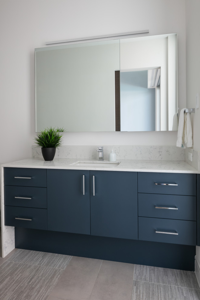 Photo of a large contemporary family bathroom in Tampa with flat-panel cabinets, blue cabinets, a built-in shower, a one-piece toilet, grey tiles, porcelain tiles, white walls, porcelain flooring, a submerged sink, engineered stone worktops, grey floors, a hinged door, white worktops, a wall niche, a single sink and a built in vanity unit.