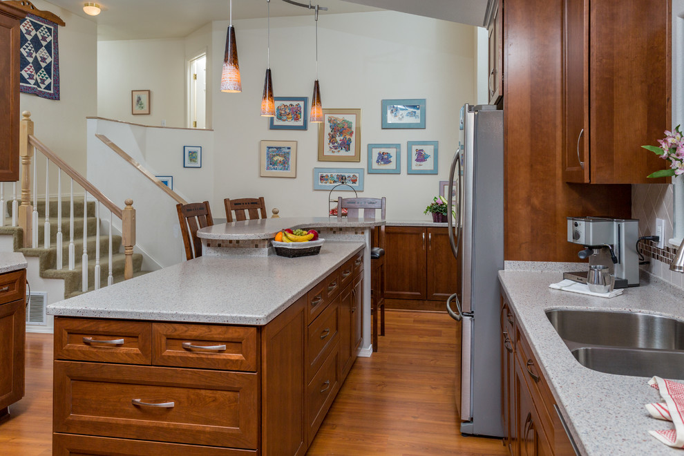 Example of a mid-sized transitional u-shaped medium tone wood floor kitchen pantry design with an undermount sink, recessed-panel cabinets, medium tone wood cabinets, solid surface countertops, beige backsplash, mosaic tile backsplash, stainless steel appliances and an island