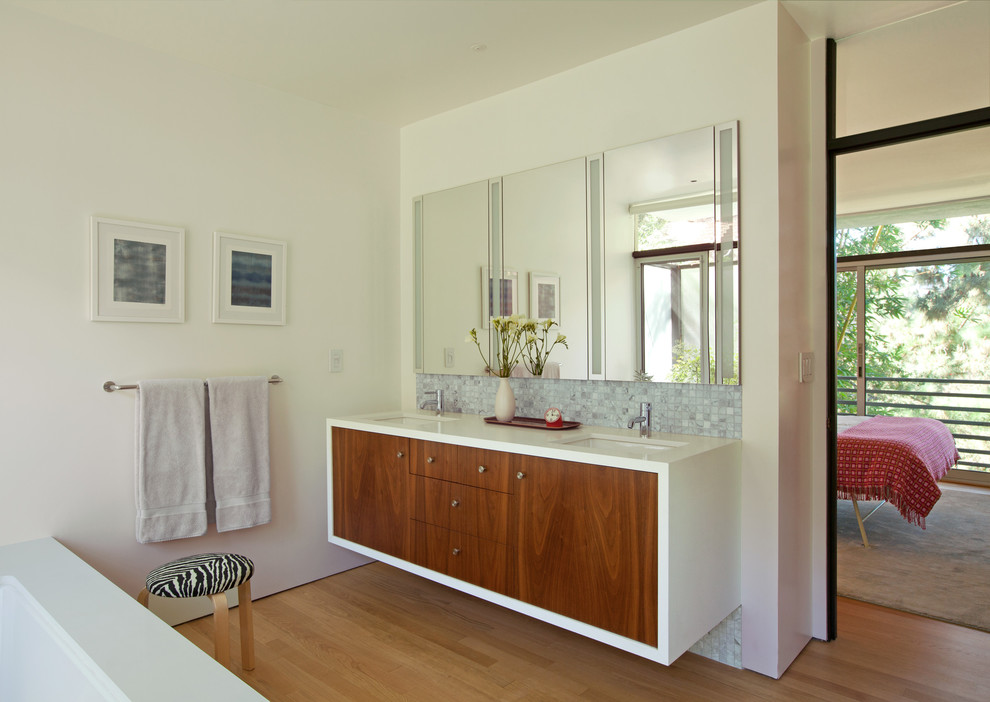 Photo of a large midcentury bathroom in Los Angeles with flat-panel cabinets, medium wood cabinets, an undermount tub, gray tile, white tile, mosaic tile, white walls, medium hardwood floors, an undermount sink, brown floor and white benchtops.
