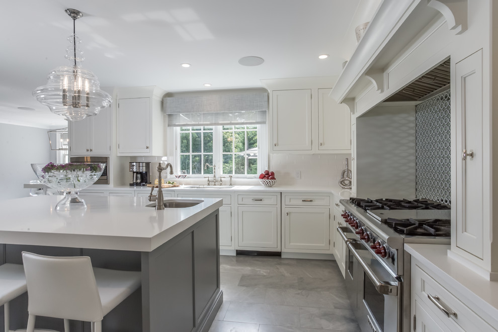 Photo of a large transitional u-shaped kitchen pantry in New York with an undermount sink, flat-panel cabinets, white cabinets, solid surface benchtops, grey splashback, glass sheet splashback, panelled appliances, marble floors, multiple islands and grey floor.