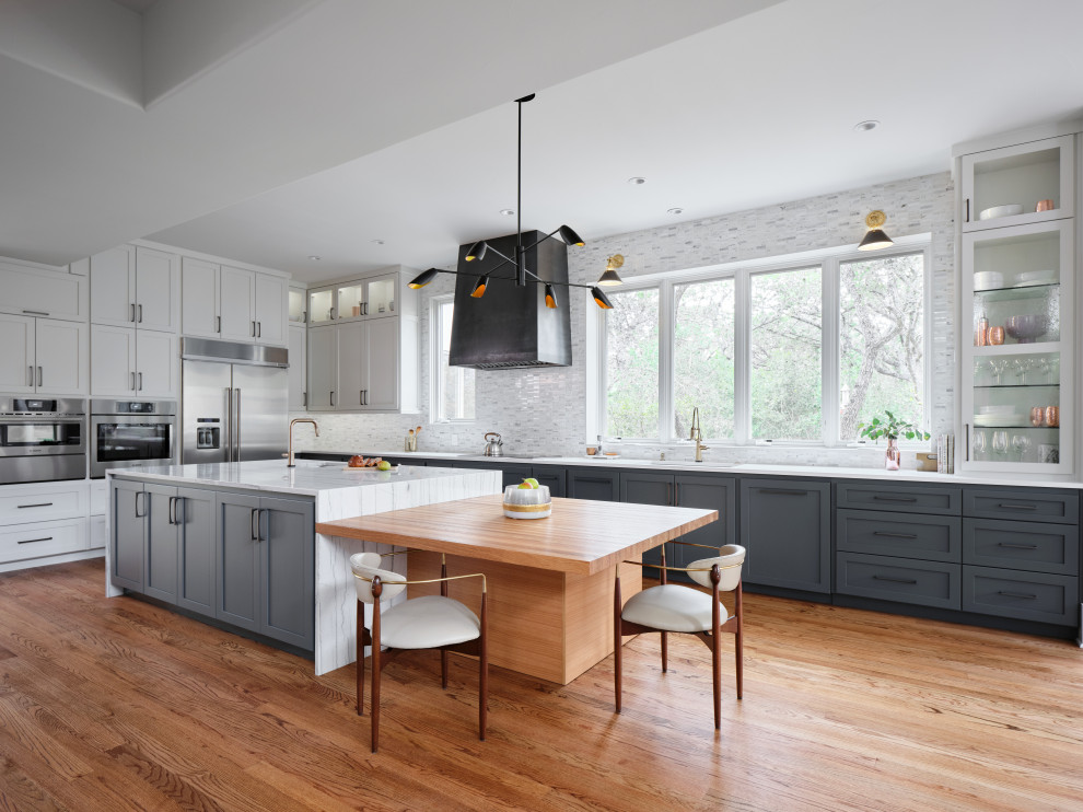 Mid-sized midcentury u-shaped eat-in kitchen in Austin with an undermount sink, shaker cabinets, blue cabinets, quartzite benchtops, white splashback, marble splashback, stainless steel appliances, medium hardwood floors, with island, brown floor and grey benchtop.