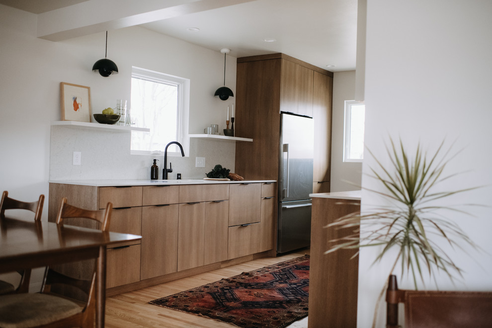 Inspiration for a scandinavian eat-in kitchen in Minneapolis with an undermount sink, flat-panel cabinets, light wood cabinets, quartz benchtops, white splashback, stainless steel appliances, light hardwood floors, no island and white benchtop.