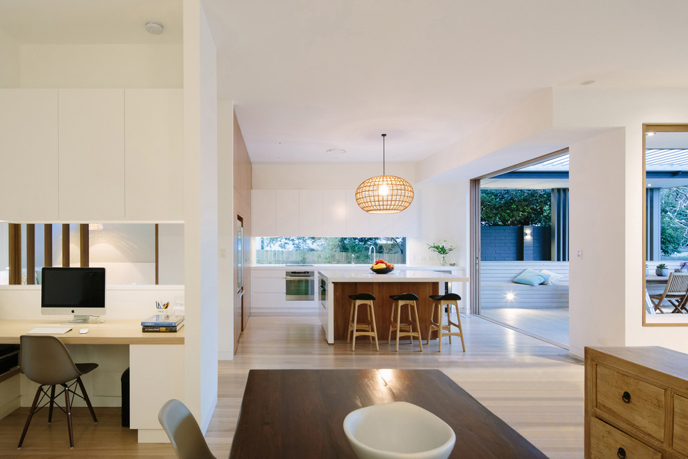 Design ideas for a mid-sized contemporary l-shaped open plan kitchen in Sydney with flat-panel cabinets, white cabinets, window splashback, stainless steel appliances, light hardwood floors and with island.