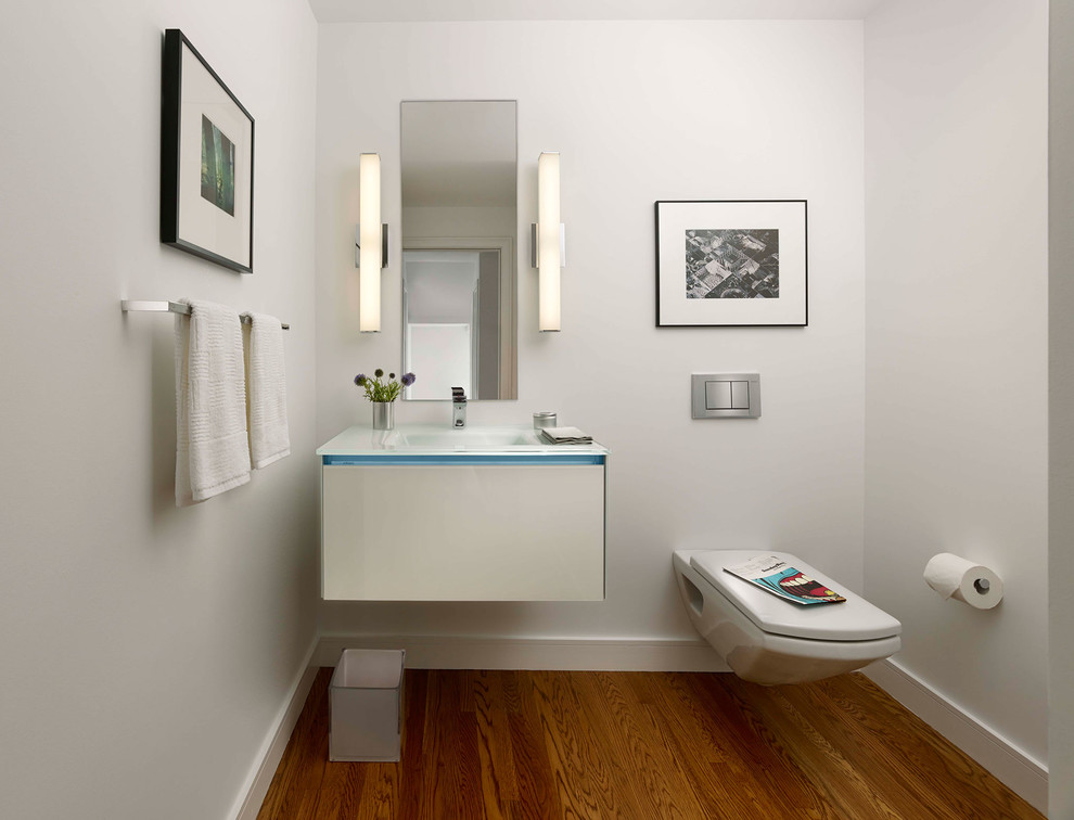 Inspiration for a small modern 3/4 bathroom in San Francisco with flat-panel cabinets, white cabinets, medium hardwood floors, a wall-mount toilet, white walls, an integrated sink and glass benchtops.