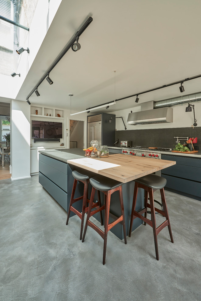 Mid-sized industrial l-shaped kitchen in London with flat-panel cabinets, grey cabinets, concrete benchtops, black splashback, stainless steel appliances, concrete floors, with island, grey floor and grey benchtop.
