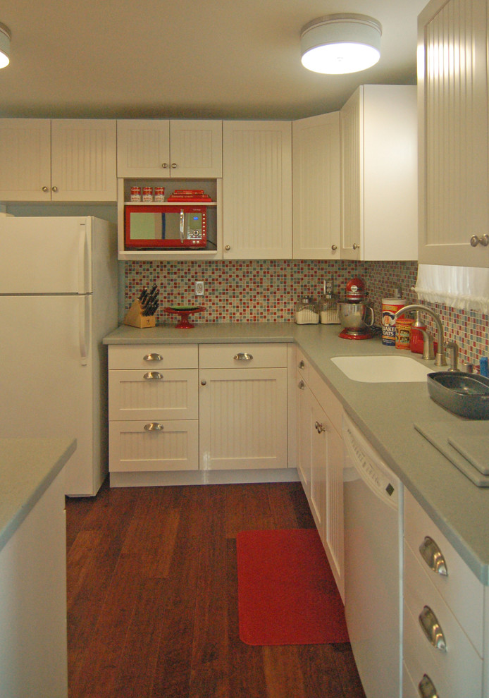 Photo of a small beach style l-shaped separate kitchen in San Luis Obispo with an integrated sink, beaded inset cabinets, white cabinets, solid surface benchtops, multi-coloured splashback, glass tile splashback, white appliances and dark hardwood floors.