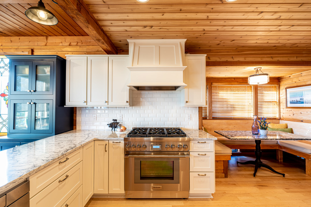 Mid-sized country u-shaped open plan kitchen in Seattle with a farmhouse sink, shaker cabinets, white cabinets, quartz benchtops, white splashback, ceramic splashback, stainless steel appliances, light hardwood floors, a peninsula, white benchtop and timber.