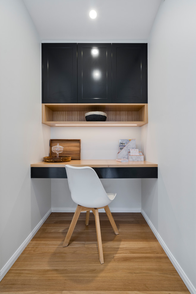 Design ideas for a small contemporary study room in Brisbane with white walls, light hardwood floors, a built-in desk and brown floor.