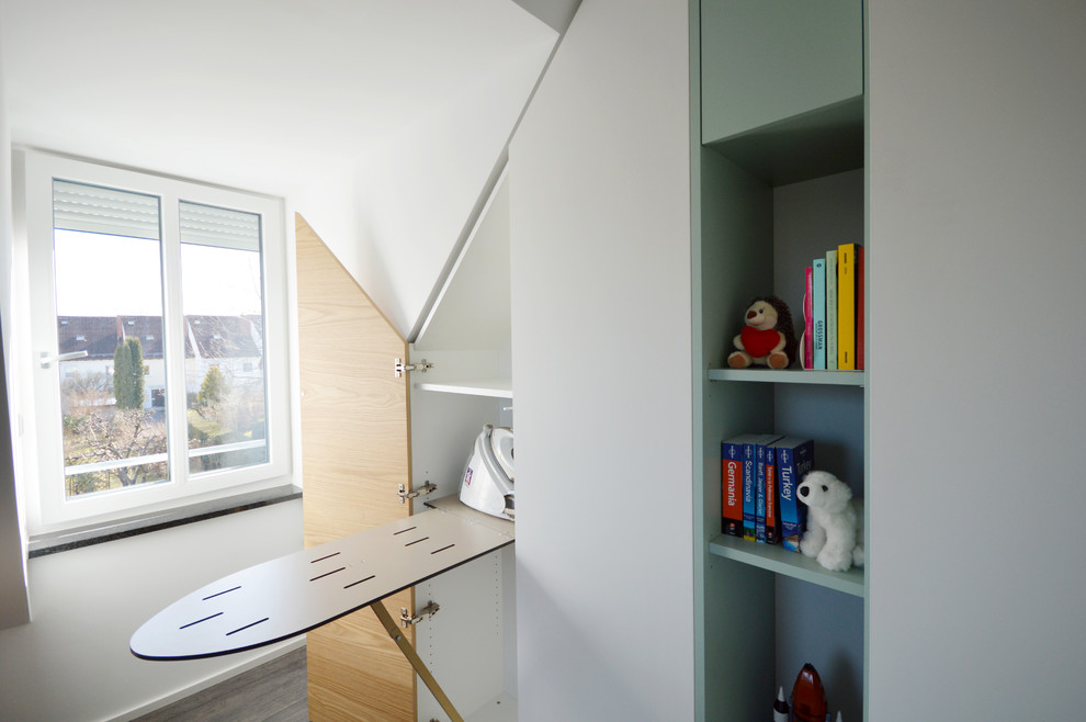 Photo of a small contemporary gender-neutral built-in wardrobe in Munich with flat-panel cabinets, white cabinets, dark hardwood floors and grey floor.