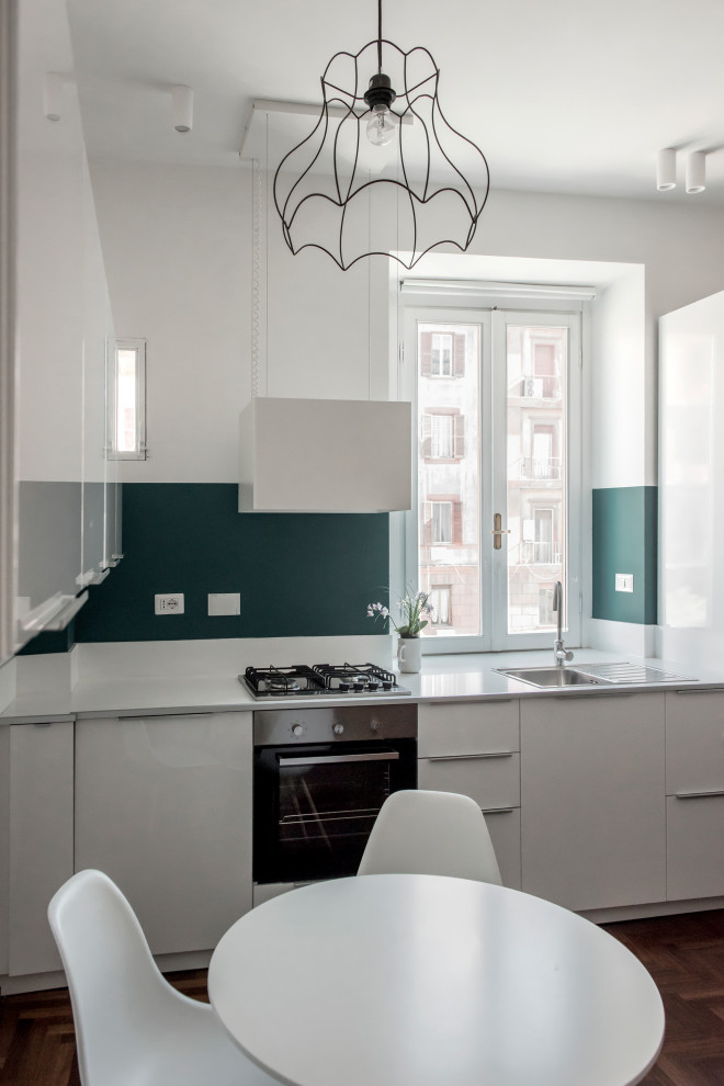 Inspiration for a small contemporary l-shaped open plan kitchen in Rome with a drop-in sink, flat-panel cabinets, white cabinets, laminate benchtops, green splashback, window splashback, stainless steel appliances, medium hardwood floors, a peninsula, brown floor and white benchtop.