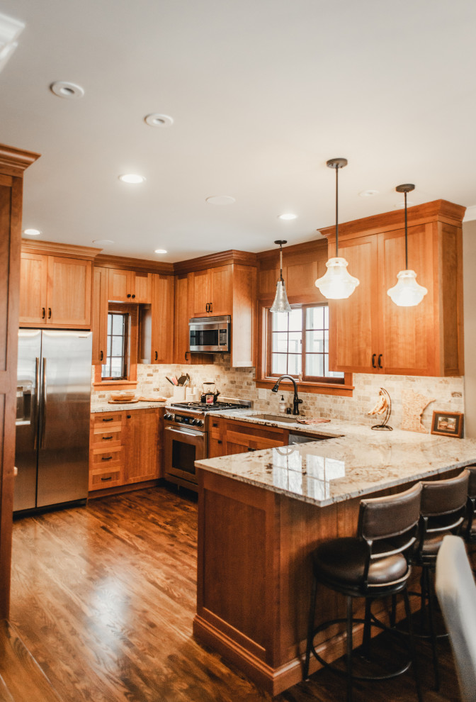 Mid-sized arts and crafts u-shaped eat-in kitchen in Minneapolis with an undermount sink, recessed-panel cabinets, medium wood cabinets, granite benchtops, beige splashback, stone tile splashback, stainless steel appliances, dark hardwood floors, a peninsula, brown floor and beige benchtop.