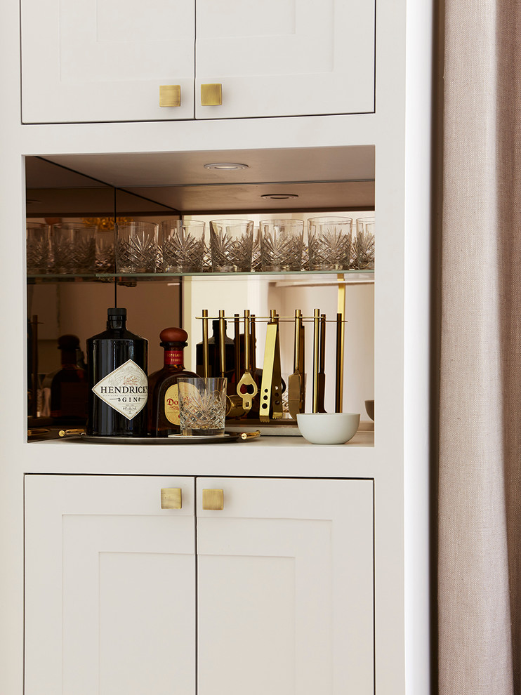 Design ideas for a transitional single-wall home bar in London with no sink, shaker cabinets, white cabinets and mirror splashback.