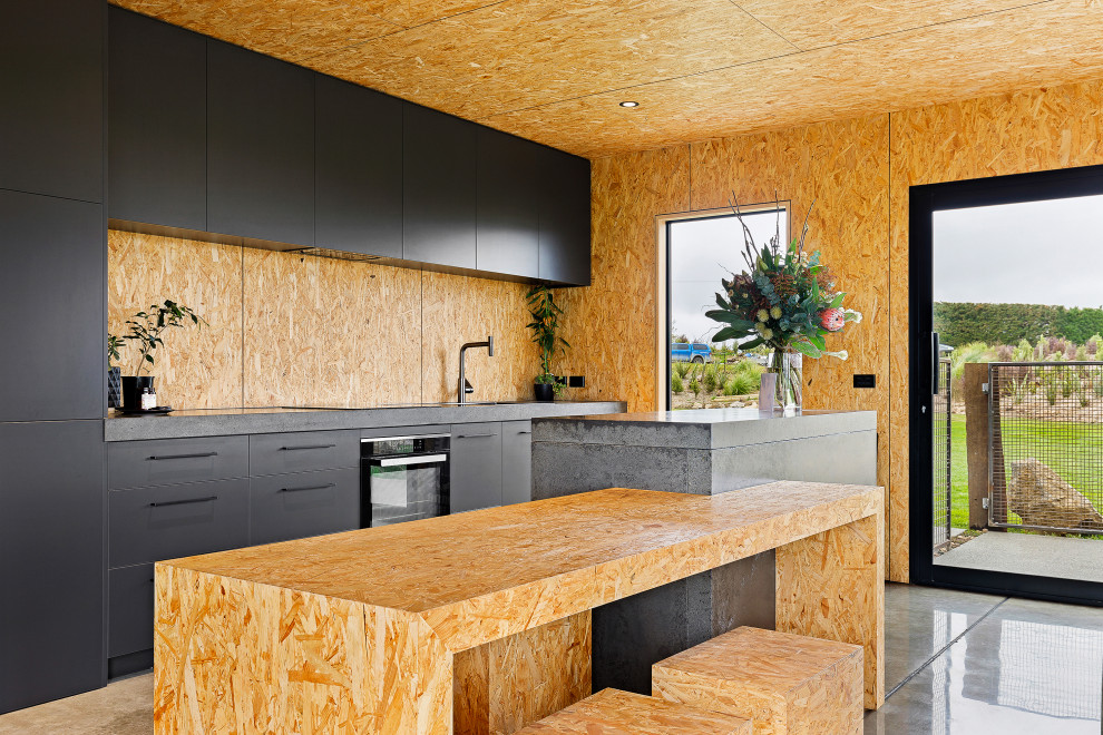 Photo of a mid-sized industrial kitchen with black cabinets, concrete benchtops, timber splashback and grey benchtop.