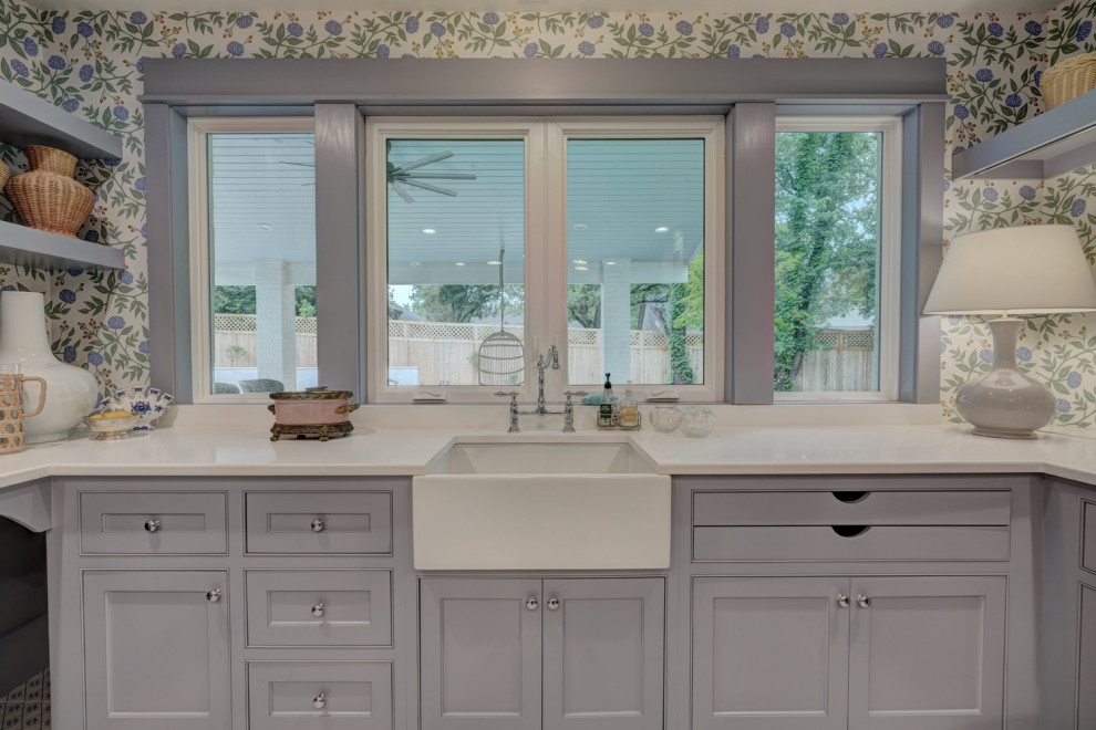 This is an example of a large traditional u-shaped utility room in Oklahoma City with a farmhouse sink, blue cabinets, quartz benchtops, porcelain floors, a side-by-side washer and dryer, blue floor, white benchtop and wallpaper.