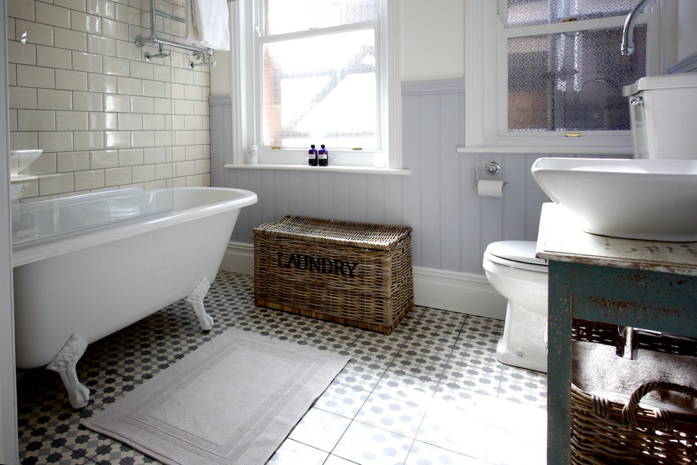 Photo of a mid-sized country bathroom in Sussex with a vessel sink, distressed cabinets, wood benchtops, a claw-foot tub, a shower/bathtub combo, beige tile and cement tile.