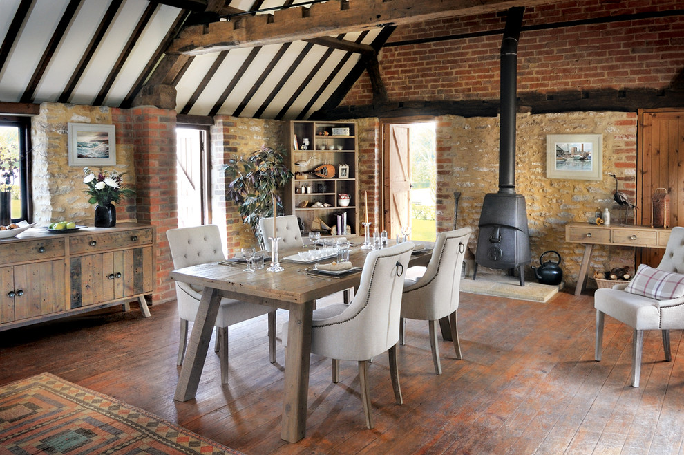 This is an example of a country dining room in Sussex with medium hardwood floors and a wood stove.
