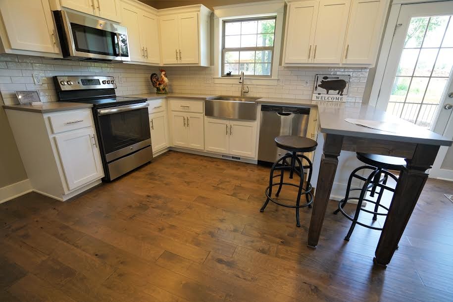 Inspiration for a large transitional u-shaped medium tone wood floor and brown floor eat-in kitchen remodel with a farmhouse sink, shaker cabinets, white cabinets, quartzite countertops, white backsplash, subway tile backsplash, stainless steel appliances and a peninsula