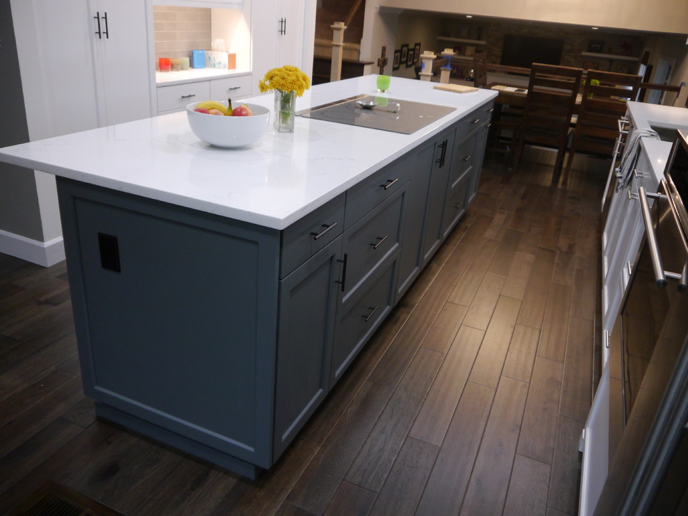Example of a large transitional dark wood floor and brown floor eat-in kitchen design in Seattle with a single-bowl sink, shaker cabinets, white cabinets, solid surface countertops, beige backsplash, ceramic backsplash, stainless steel appliances, an island and white countertops