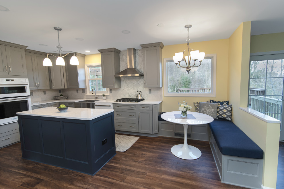 Inspiration for a large transitional u-shaped eat-in kitchen in Baltimore with a farmhouse sink, recessed-panel cabinets, grey cabinets, quartzite benchtops, white splashback, subway tile splashback, white appliances, dark hardwood floors, with island, brown floor and white benchtop.