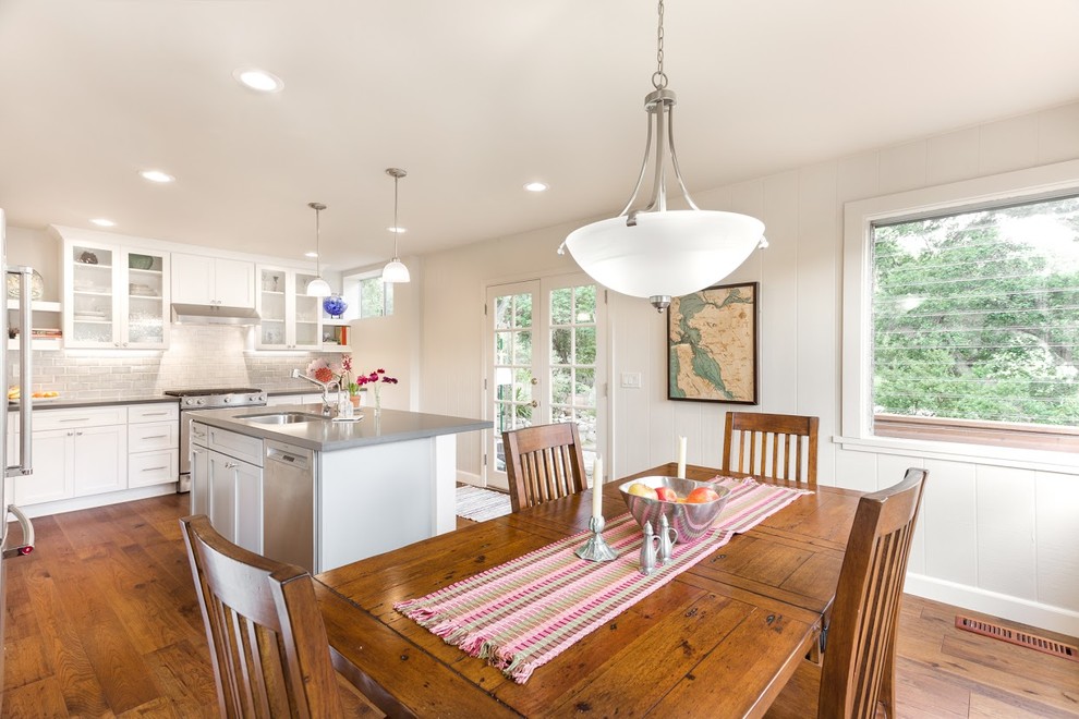 Example of a mid-sized transitional l-shaped medium tone wood floor eat-in kitchen design with an undermount sink, flat-panel cabinets, white cabinets, quartz countertops, gray backsplash, ceramic backsplash, stainless steel appliances and an island